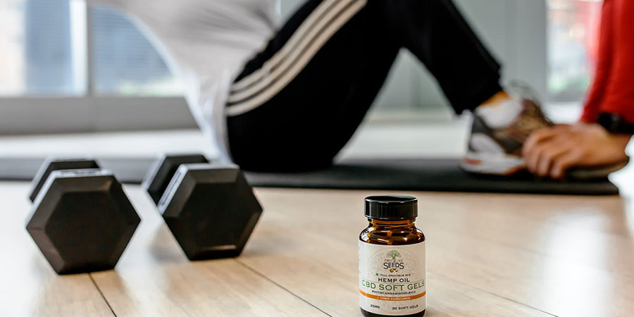 a woman doing situps, two black dumbbells and a bottle of CBD soft gels on the floor