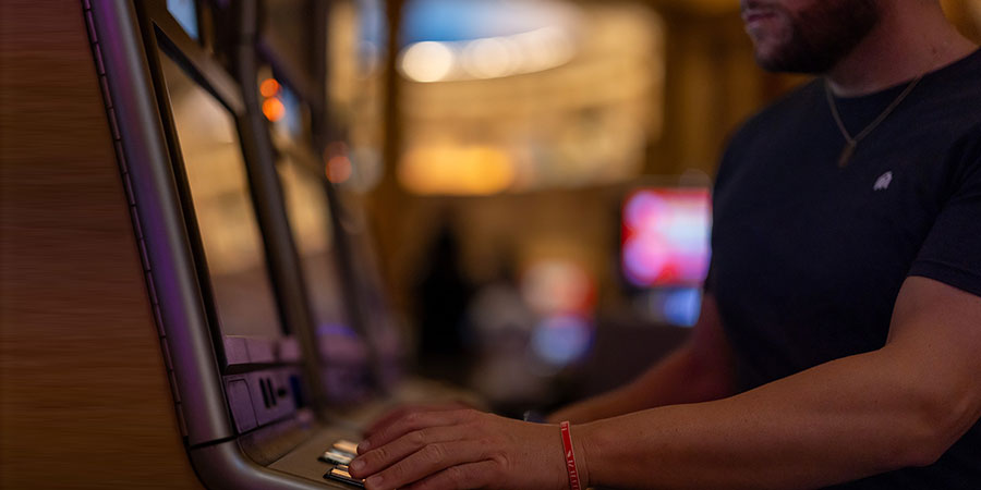 man wearing a necklace and navy blue t-shirt and playing with a slot machine